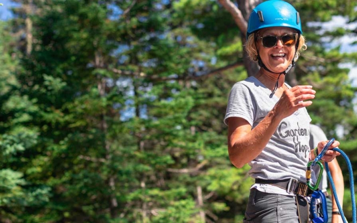 A person wearing safety gear smiles at the camera. There are green trees behind them.